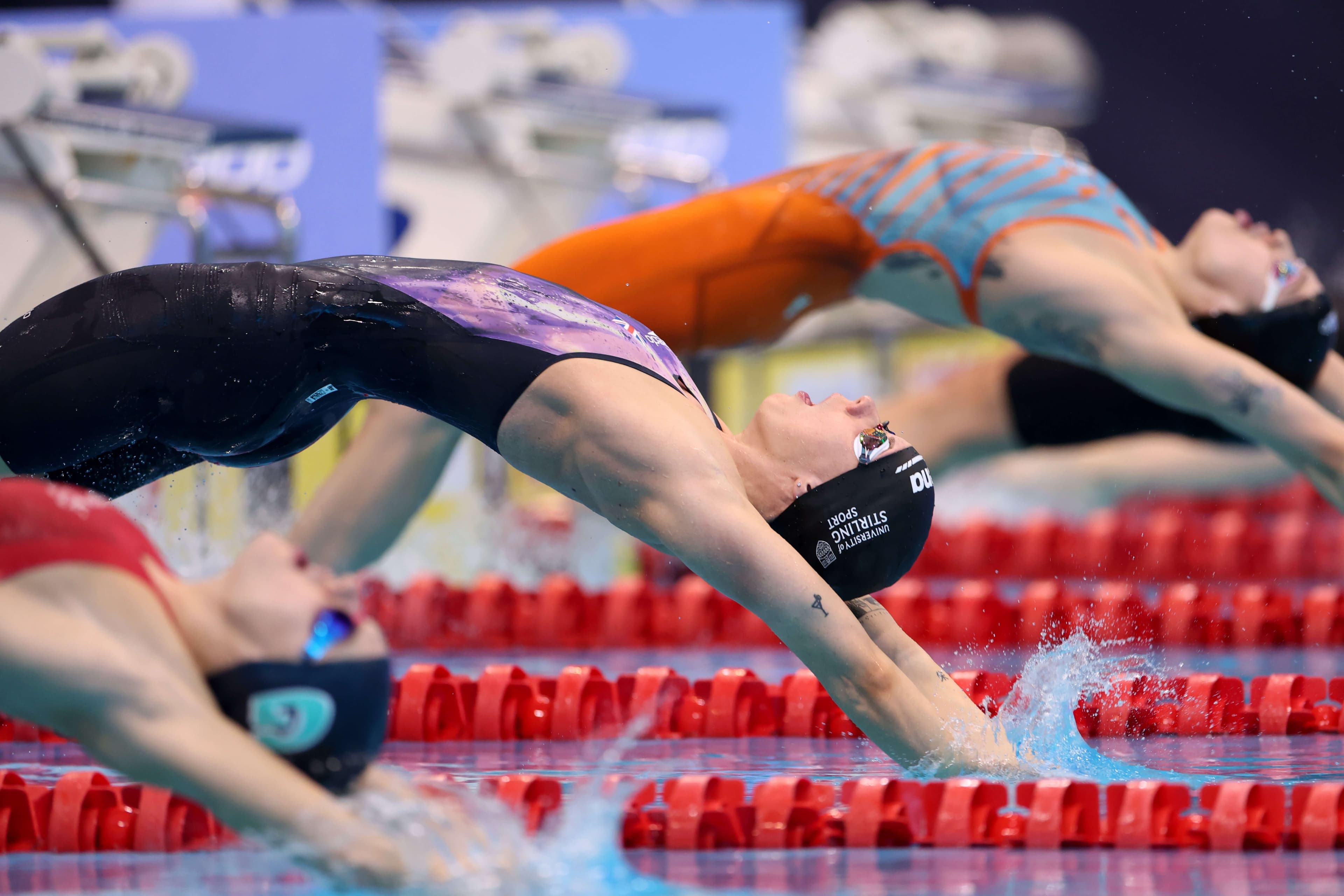 Swimmers diving into the pool backwards for backstroke race